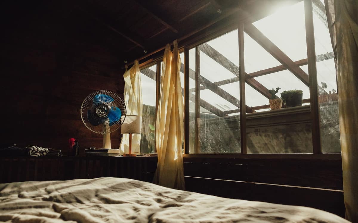 A bedroom fan standing beside a neatly made bed