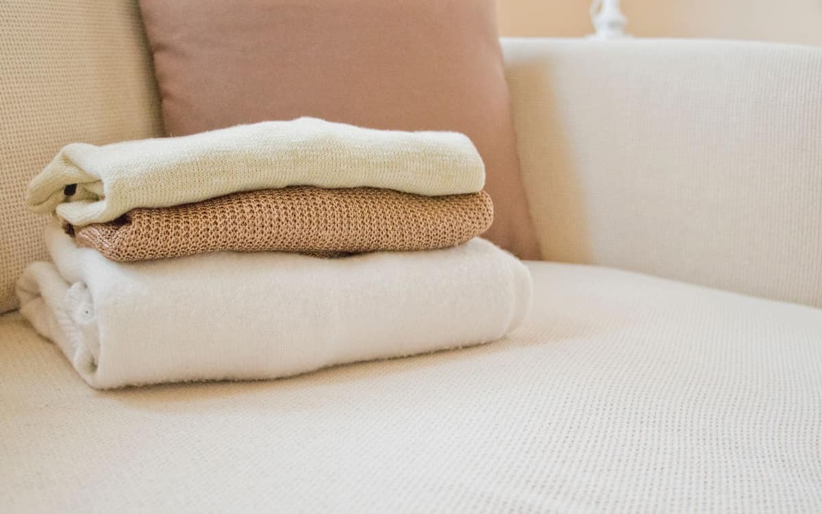 Folded blankets in several different weaves stacked on a sofa