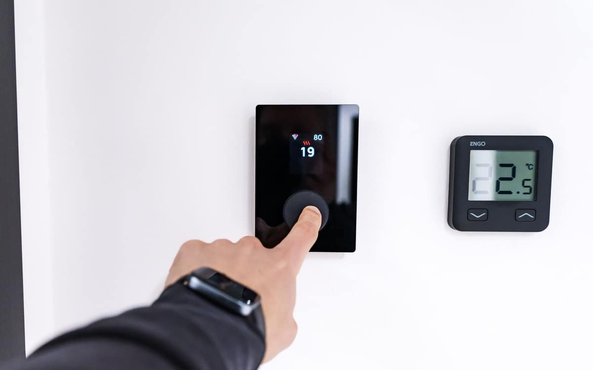 A hand setting the temperature on a digital wall thermostat