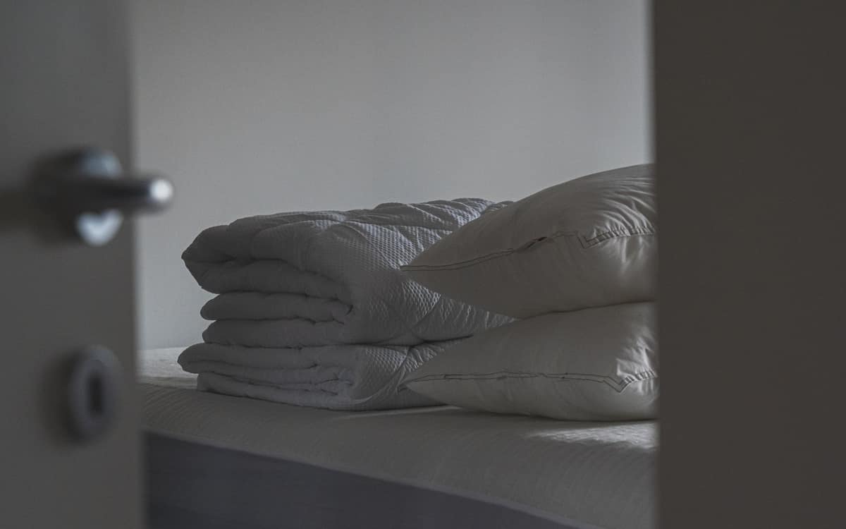 Two stacked white bed pillows beside a folded quilt on a bare mattress