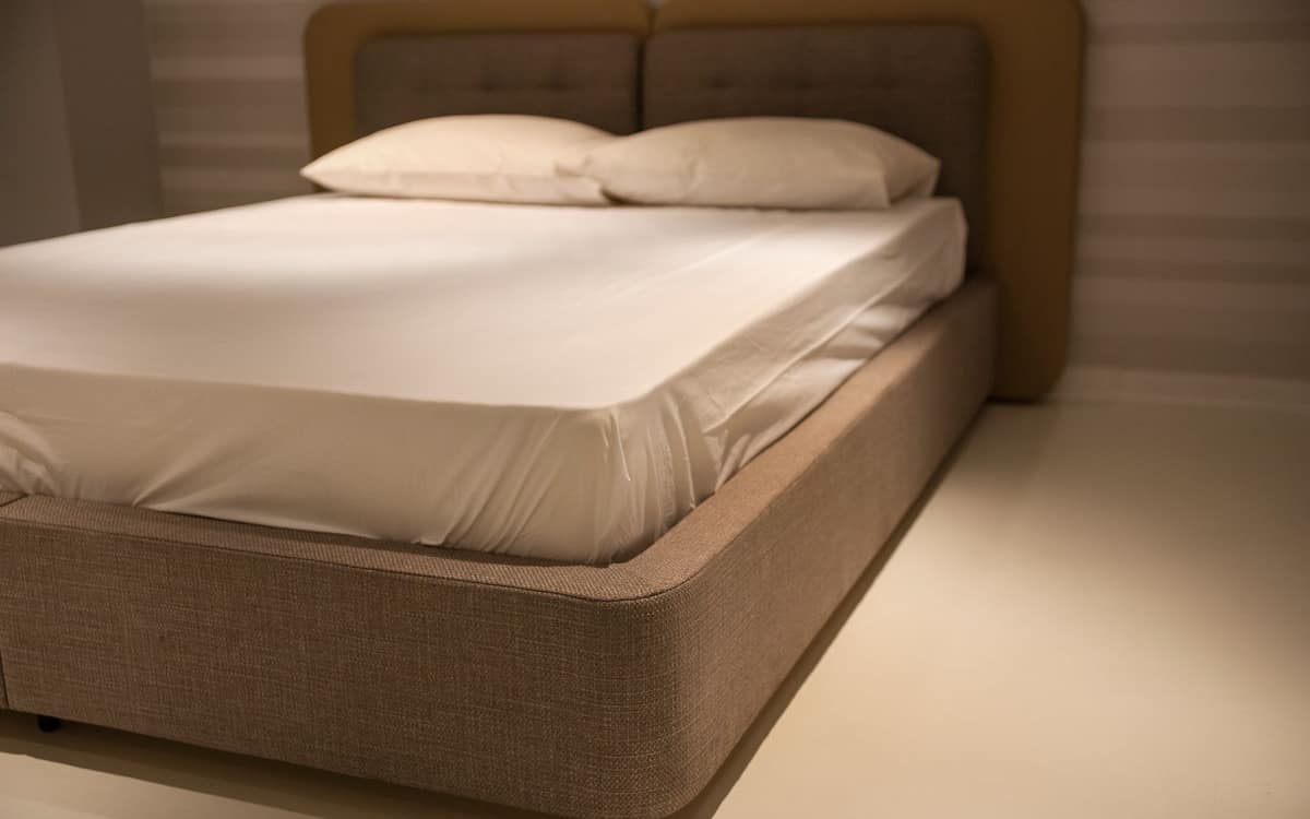 A bare mattress under a smooth fitted cover on a bed base