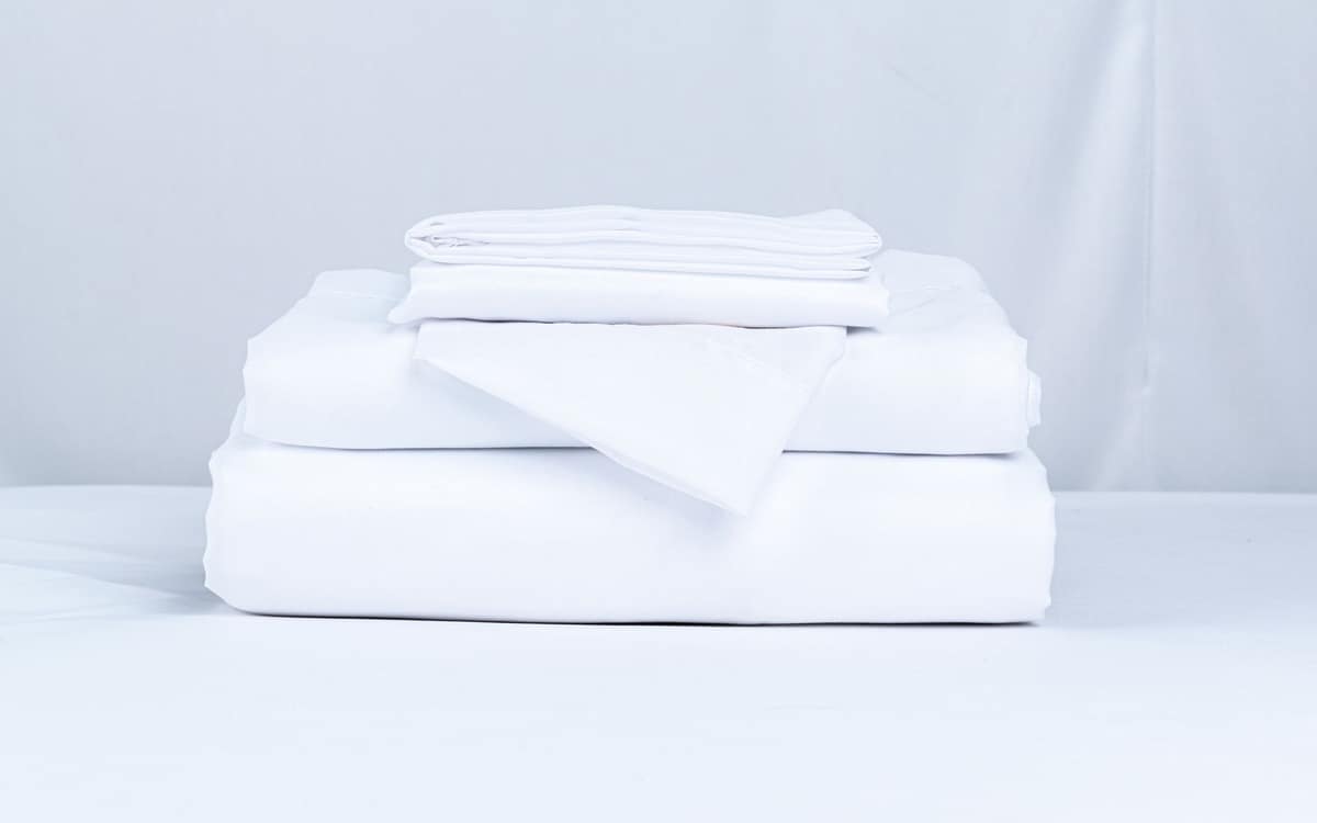 A stack of folded, clean white bed sheets