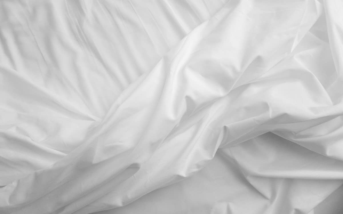 Smooth white satin-finish sheets rumpled on a bed