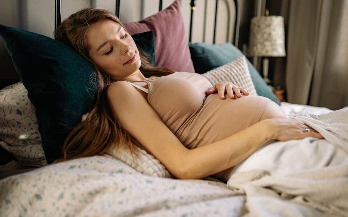 A pregnant woman resting propped up on pillows in bed