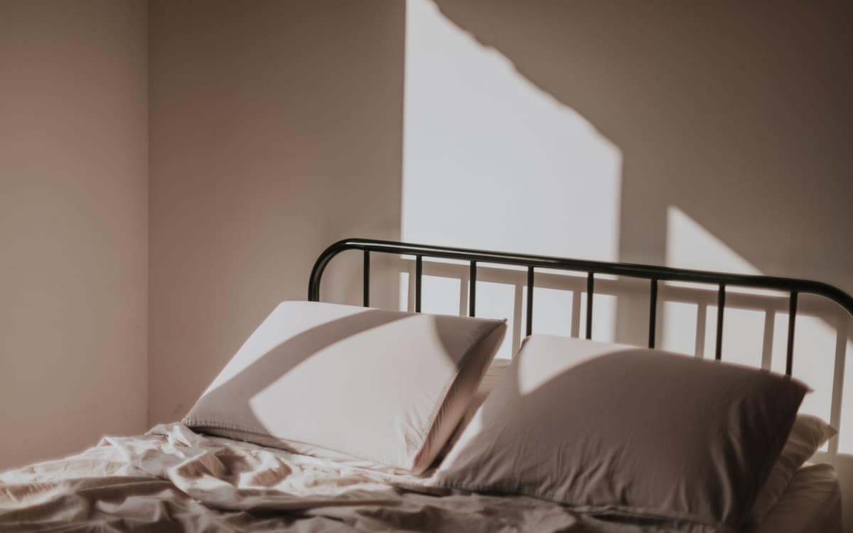 A firm, neatly made bed in a plain bedroom