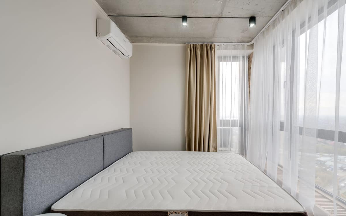 A bare mattress on a bed frame in a bright, empty bedroom