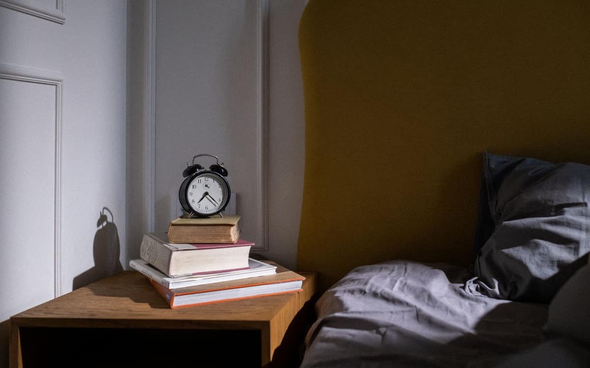 An alarm clock and books on a nightstand beside a bed