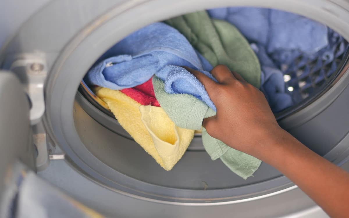 A hand loading laundry into a front-loading washing machine
