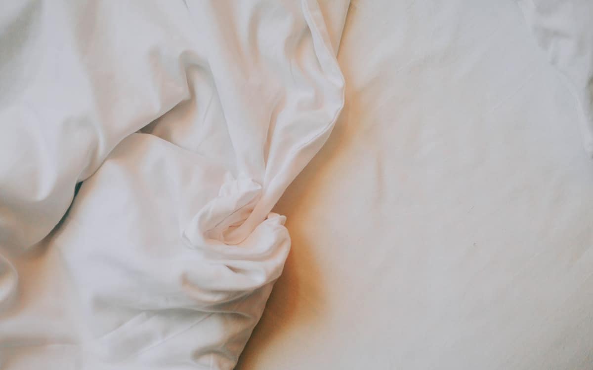 A worn, crumpled white bed sheet in soft light